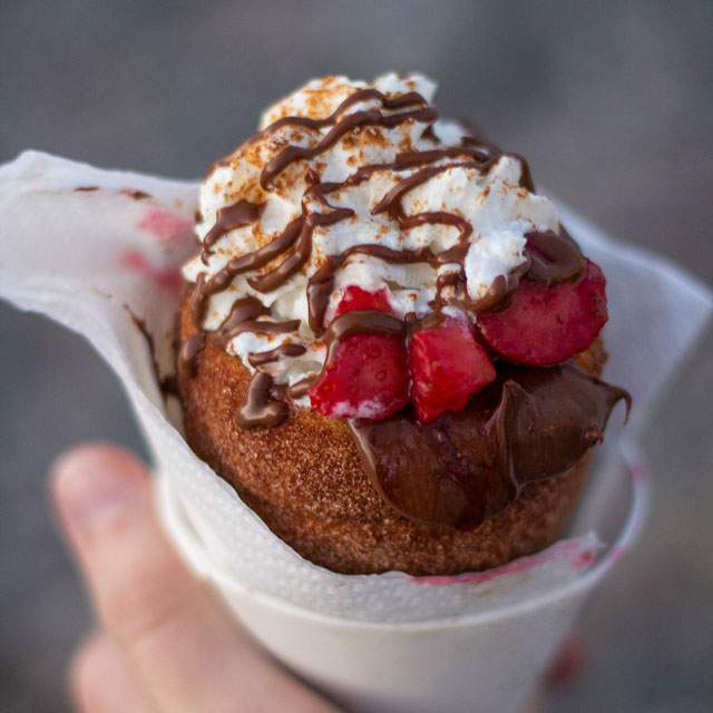Baked cinnamon dough cone filled with Nutella, topped with strawberries, whipped cream, and chocolate syrup